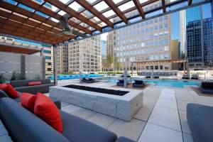 Roof top public area showing outdoor upholstered sofa in front of a fire pit. Downtown Minneapolis buildings are in the background.
